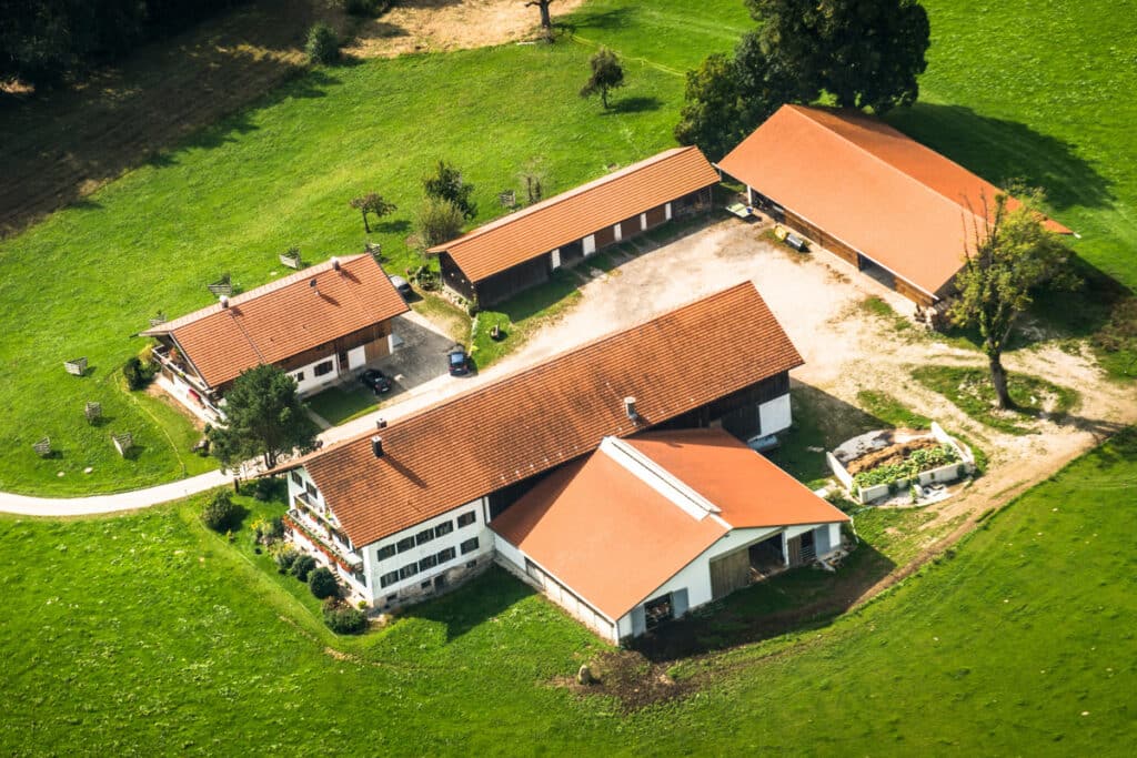Corps de Ferme Traditionnel: Vue Aérienne sur un Domaine Rural Vue aérienne d'un corps de ferme traditionnel avec toits tuilés rouges, maisons, granges et champs verts ensoleillés.