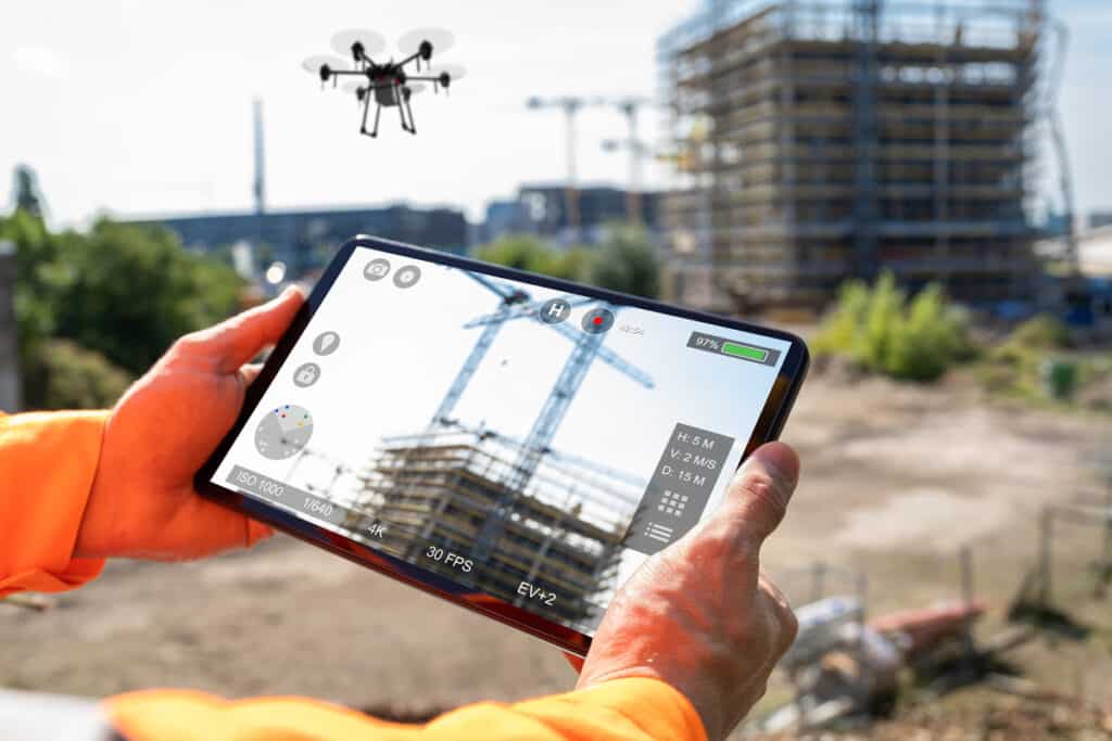 Personne en orange contrôle un drone via tablette sur chantier. Écran affiche vidéo 4K, H: 5M, 97% batterie.