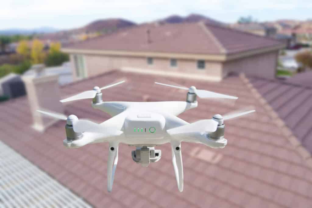 Drone blanc en vol au-dessus de toits résidentiels, son indicateur de batterie affichant trois barres vertes.