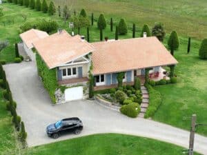 Maison provençale au toit de tuiles avec jardin paysager, vigne vierge et voiture noire garée dans l'allée.