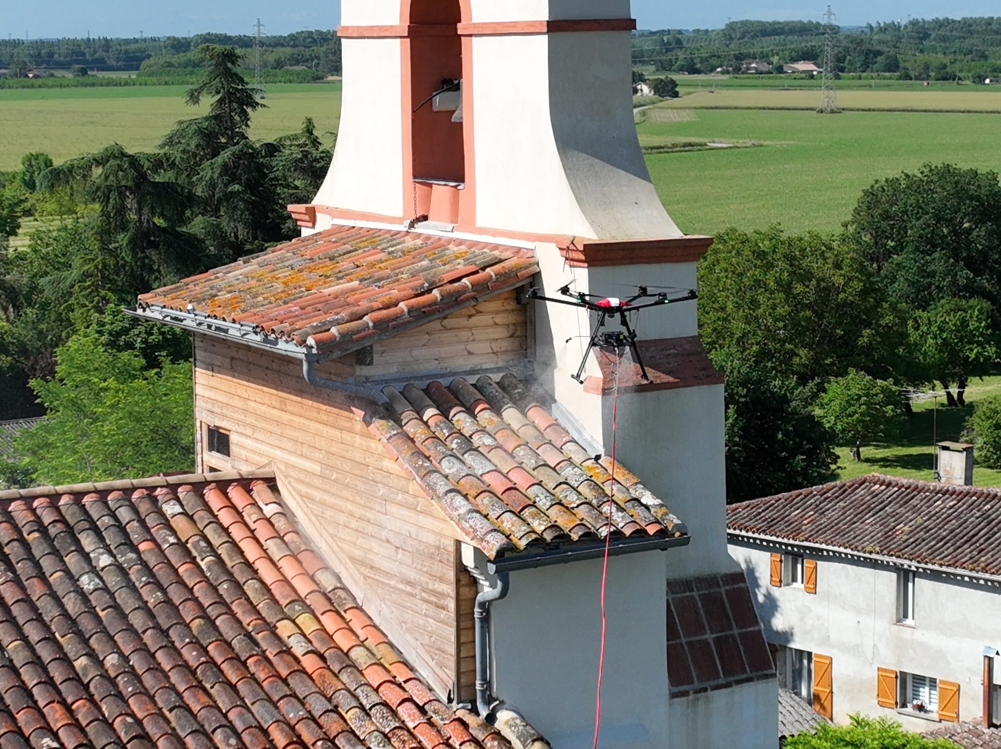 Drone professionnel nettoyant un toit de tuiles d'un clocher avec un jet de pulvérisation.